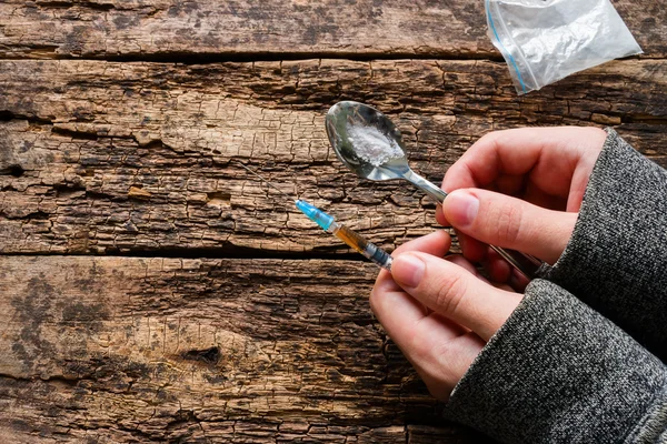 Drogadicto sosteniendo cuchara con la droga en la mano y una jeringa sobre un fondo de madera — Foto de Stock