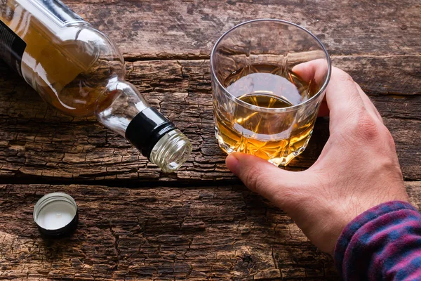 Alcoholic sosteniendo un vaso de alcohol junto a una botella vacía — Foto de Stock