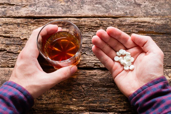 Hombre sosteniendo un vaso de alcohol y un puñado de pastillas — Foto de Stock