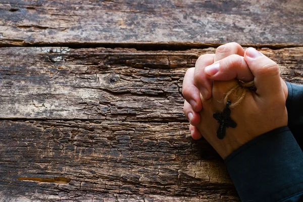 Uomo che prega con una croce tra le mani sullo sfondo di legno con spazio per il testo — Foto Stock