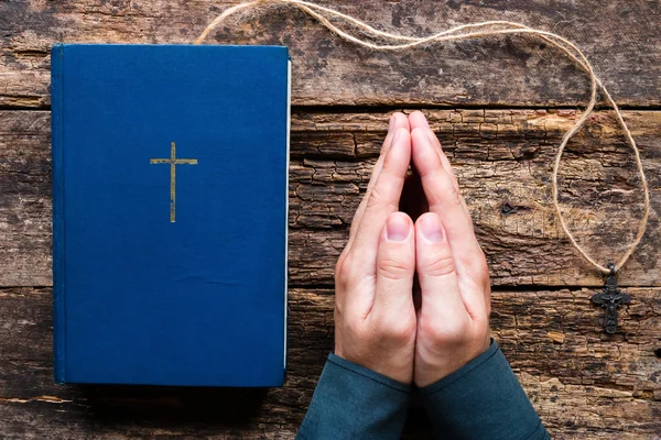 Uomo che prega accanto alla Bibbia e croce su uno sfondo di legno — Foto Stock