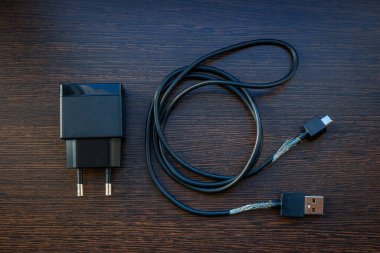 Ahşap arka planda çıplak kabloları olan akıllı telefon için eski mobil şarj kablosu