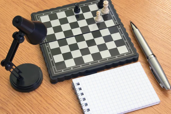 Lámpara de ajedrez cuaderno y pluma en la mesa — Foto de Stock