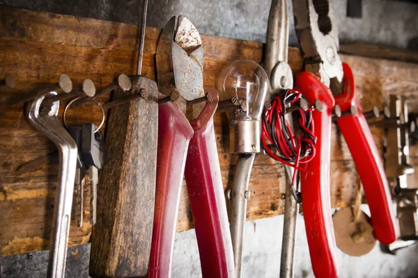 Wrenches, pliers, bulbs, pliers, wire, rope on the nails on the old wooden stand side view close-up — Stockfoto