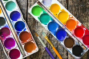 Two watercolor paints and different brushes for drawing on an old wooden table