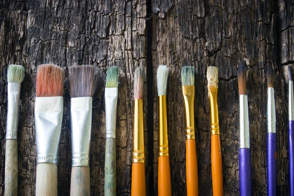 Paint brushes of different sizes have different colors in a row horizontally on an old wooden table — Zdjęcie stockowe