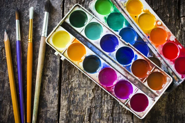 Two watercolor paint and pencil, different fan brush to paint on an old wooden table — Stok fotoğraf