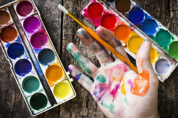 Watercolor paint brush to paint the hand of the artist in multi-colored paint on wood background holding a brush — Zdjęcie stockowe