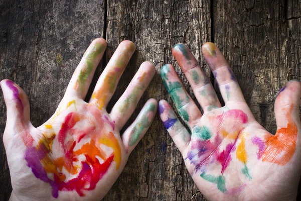 La mano del artista en pintura acuarela de colores manchados sobre un fondo de una mesa de madera — Foto de Stock