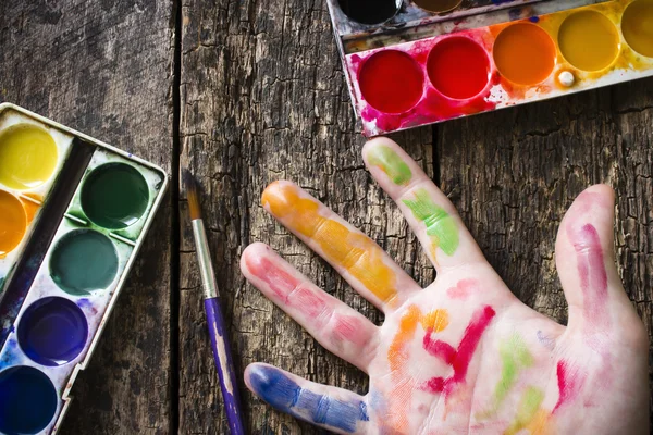 Mano del artista junto al pincel para dibujar sobre un fondo de mesa vieja, enfoque selectivo acuarela — Foto de Stock