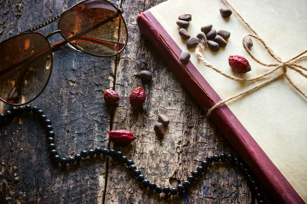 Glasses, beads, books, nuts, dog-rose on a wooden background — Stockfoto