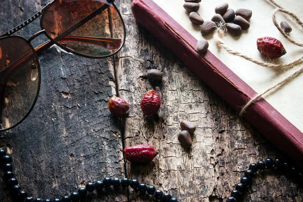 Glasses, beads, books, nuts, rose hips on a wooden background closeup — Stockfoto