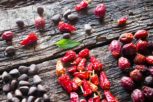 Leaf, pine nuts, dried red peppers and wild rose on a wooden background selective focus — Stock Photo, Image