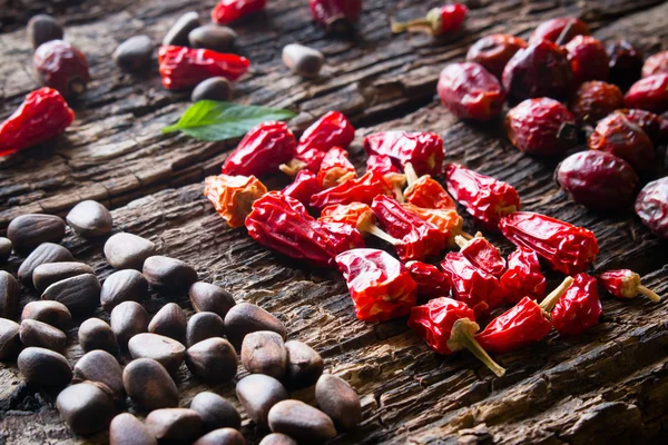 Leaf, pine nuts, dried red peppers and wild rose on wooden background close-up selective focus — Stock Photo, Image