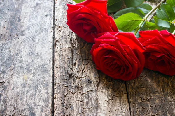 Three red roses on a wooden background with the stem and leaves — Stock Photo, Image