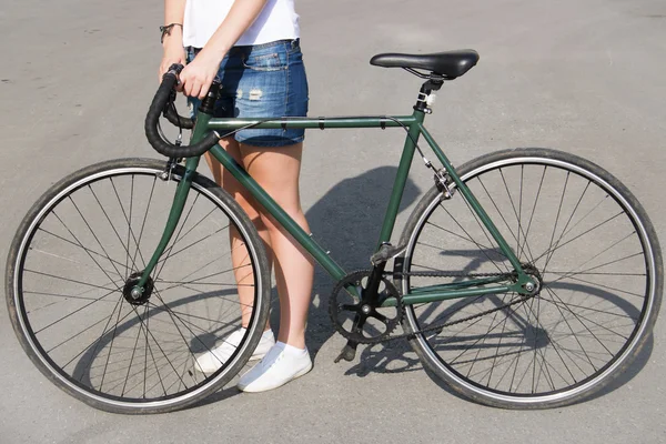 Yolun yanındaki yeşil bisiklet üzerinde duran genç kadın — Stok fotoğraf