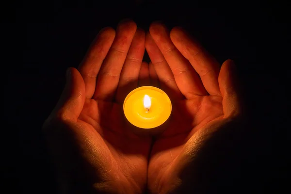 Hands in the shape of a heart holding a lighted candle on a black background — Stock Photo, Image