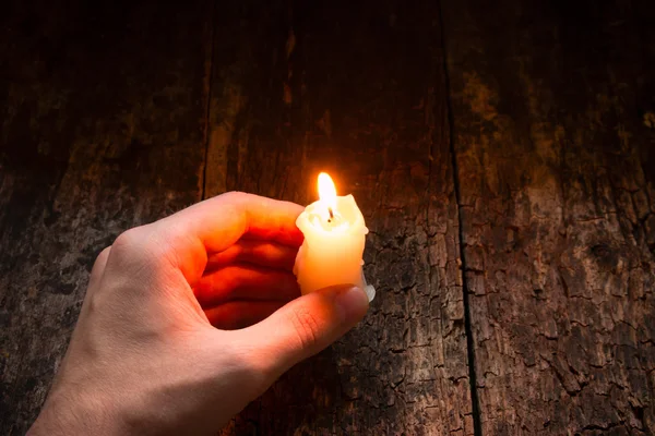 Man holding in his hand a lighted wax candle on a wooden background — Stock Photo, Image