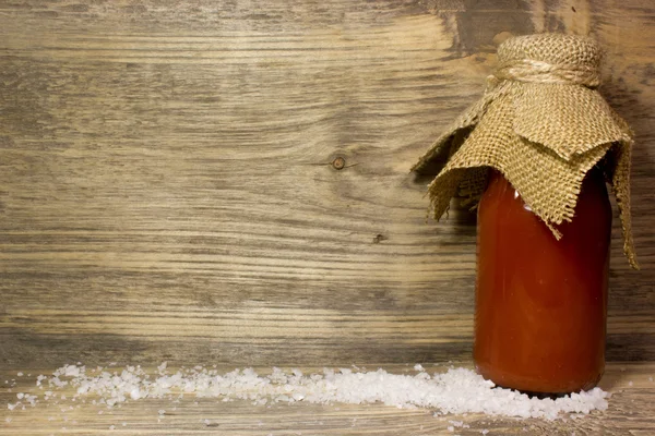 Tomato juice in glass bottle and big sea salt on wooden background — Stock Photo, Image