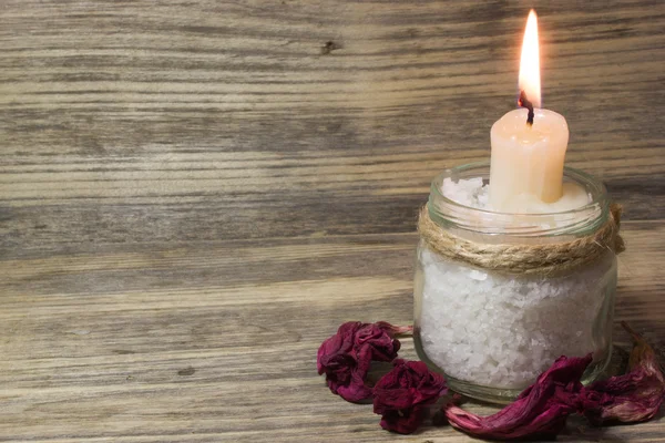 Burning white candle in glass jar on wooden background