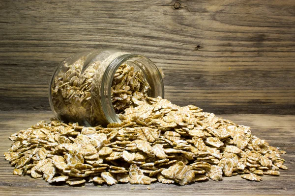 Пшеничні пластівці в скляній банці на дерев'яному фоні — стокове фото