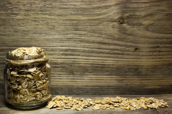 Пшеничні пластівці в скляній банці на дерев'яному фоні — стокове фото