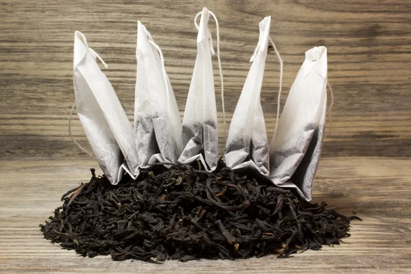 Dry tea leaves for black tea and paper tea bag on wooden background