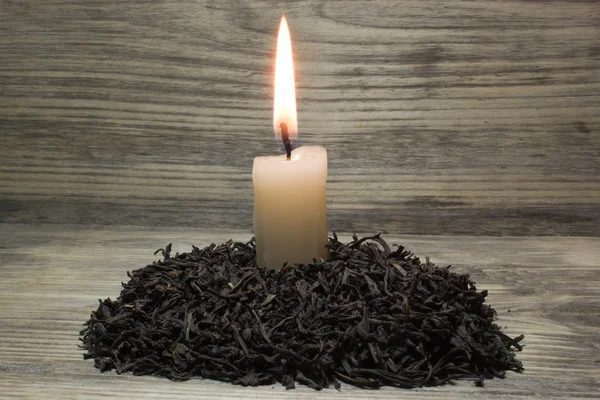 Hojas de té secas para té negro y vela encendida sobre fondo de madera — Foto de Stock
