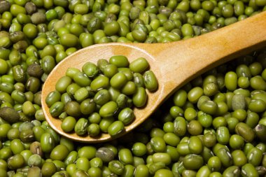 Green mung beans and wooden spoon on a wooden background clipart