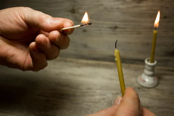 Una cerilla encendida en su mano y la vela, Partidos con cabezas azules sobre fondo de madera — Foto de Stock