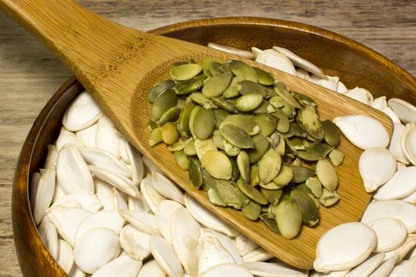Pumpkin seeds and wooden spoon on wooden background — Stock Photo, Image