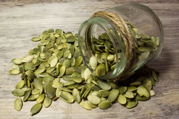 Pumpkin seeds and jar on wooden background — Stock Photo, Image