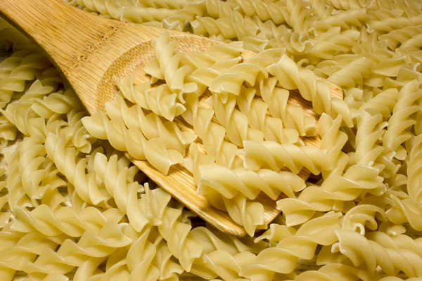 Fideos en espiral y cuchara de madera sobre fondo de madera — Foto de Stock