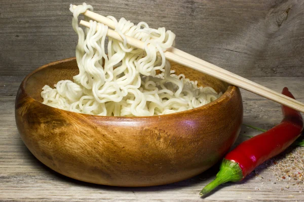 在一个木碗用筷子的方便面。木制的背景和红辣椒. — 图库照片