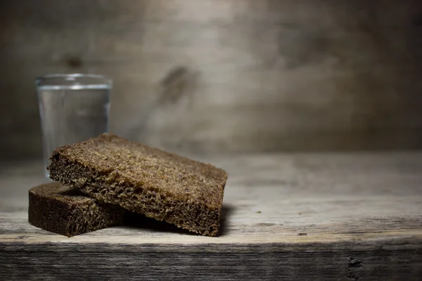 Un vaso de vodka y una rebanada de pan de centeno en una mesa de madera . — Foto de Stock