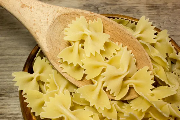 Tallarines Farfalle mariposas y cuchara de madera sobre fondo de madera . — Foto de Stock