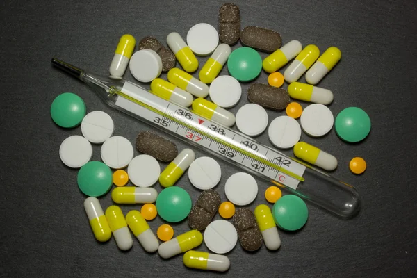 Медицинский термометр и таблетки на тёмном фоне — стоковое фото