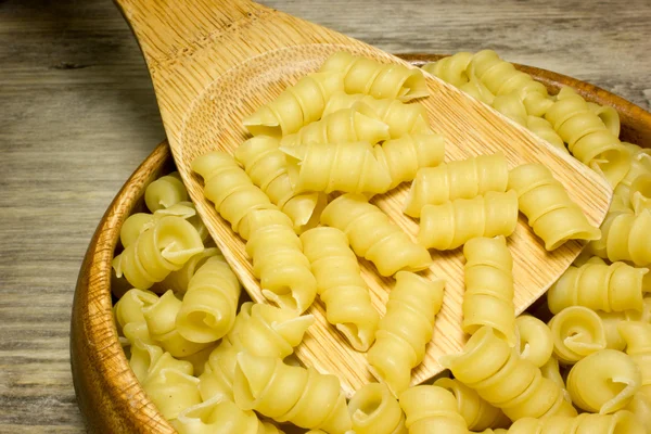 Fideos en espiral y cuchara sobre fondo de madera — Foto de Stock