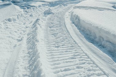 Derin karda kar motosikleti izleri. Karla kaplı bir araziyi geçen bir kar aracının çarpık izleri.