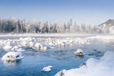 Sisli yüzeyi olan kışın manzarası. Nehir kıyısındaki kayalar ve ağaçlar karla kaplı..