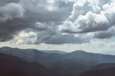 Dağların üzerinde kalın bulutlar, mavi sisli tepeler.