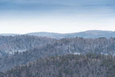 Orman tepelerinin yumuşak yamaçları ilk karla kaplıdır. Ufuktaki dağ vadileri ve tepe manzarası.