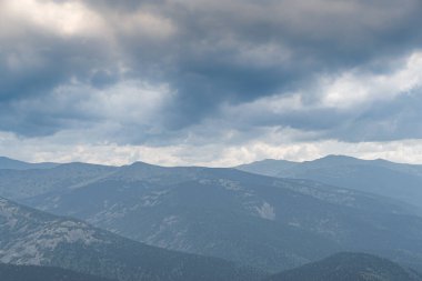 Dağların üzerinde kalın bulutlar, mavi sisli tepeler.