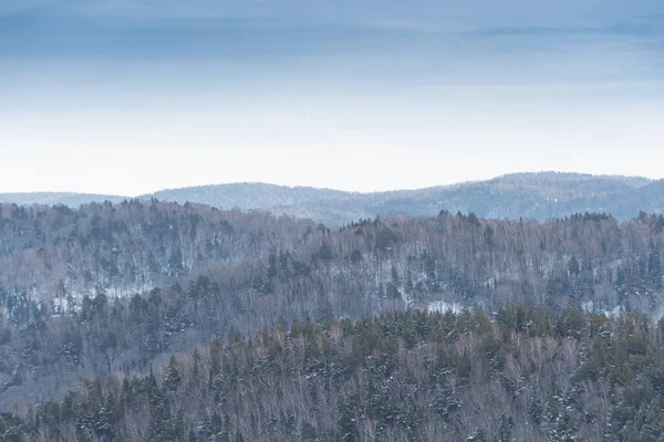Orman tepelerinin yumuşak yamaçları ilk karla kaplıdır. Ufuktaki dağ vadileri ve tepe manzarası.
