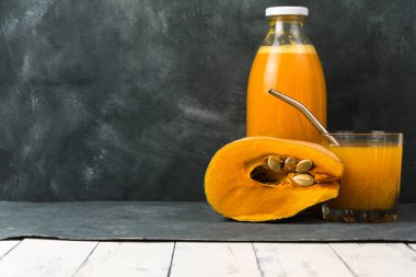 Bir şişe ve koyu arkaplanda taze sıkılmış balkabağı suyu. Vejetaryen için sağlıklı yiyecek ve içecekler. Tohumlu bir parça taze balkabağı..