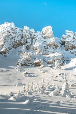 Kayalık kayalıklar mavi gökyüzünün altında karla kaplıdır. Dağcılık için buzdaki sıradağlar zordur. Buzlu ayak ağaçlarında. Yol zirveye çıkar. Kışın dikey manzarası