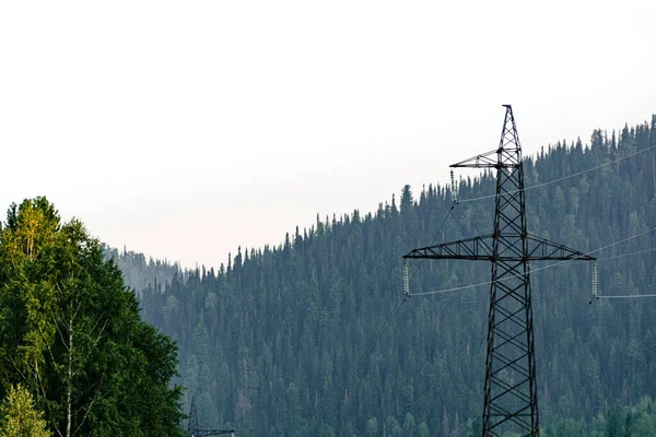 Power transmission tower in mountainous area on background of a forest hill. Electrification of rural areas.