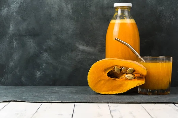 Bir şişe ve koyu arkaplanda taze sıkılmış balkabağı suyu. Vejetaryen için sağlıklı yiyecek ve içecekler. Tohumlu bir parça taze balkabağı..