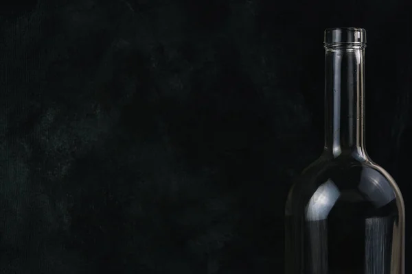 Long necked bottle of wine against dark wall. Silhouette of bottle is illuminated. Free space for text