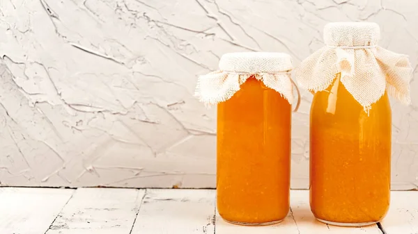 Two bottles of orange drink against concrete wall on wooden plank table. Space for text. Freshly squeezed vegetable juice in bottles for transport. Fitness food, farm product